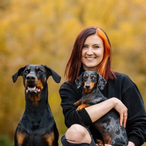 Hundetrainerin Sophia Bauer und ihre Hunde Bambi und Maya sitzen im freien vor herbstlichem Hintergrund.